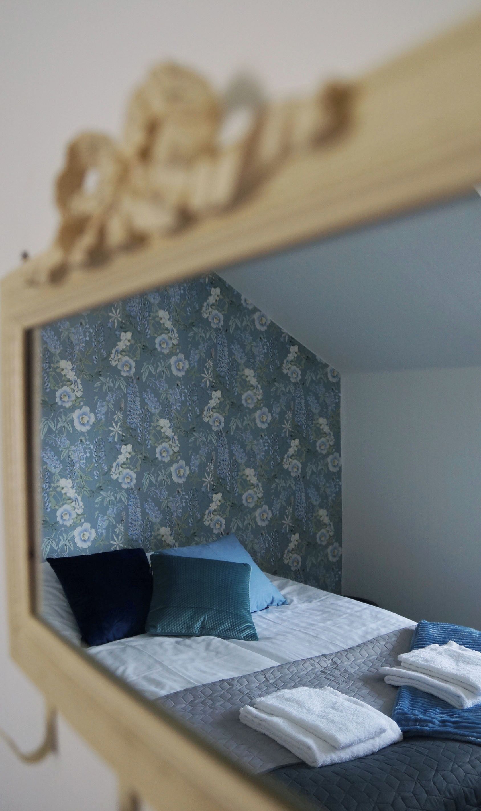A bed with a quilted gray mattress, blue and teal pillows, and a floral-patterned headboard.