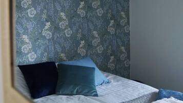 A bed with a quilted gray mattress, blue and teal pillows, and a floral-patterned headboard.