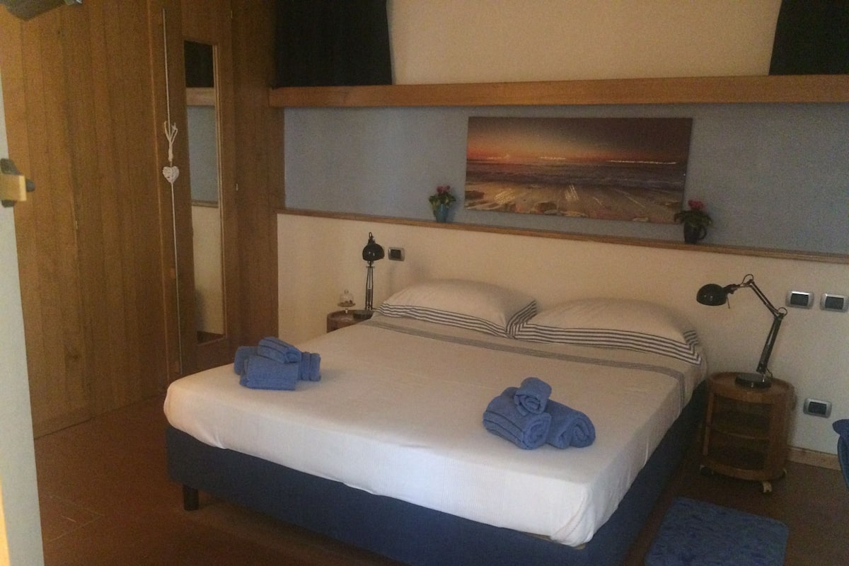 Een slaapkamer met een bed, twee nachtkastjes, een schilderij aan de muur en een blauw vloerkleed.