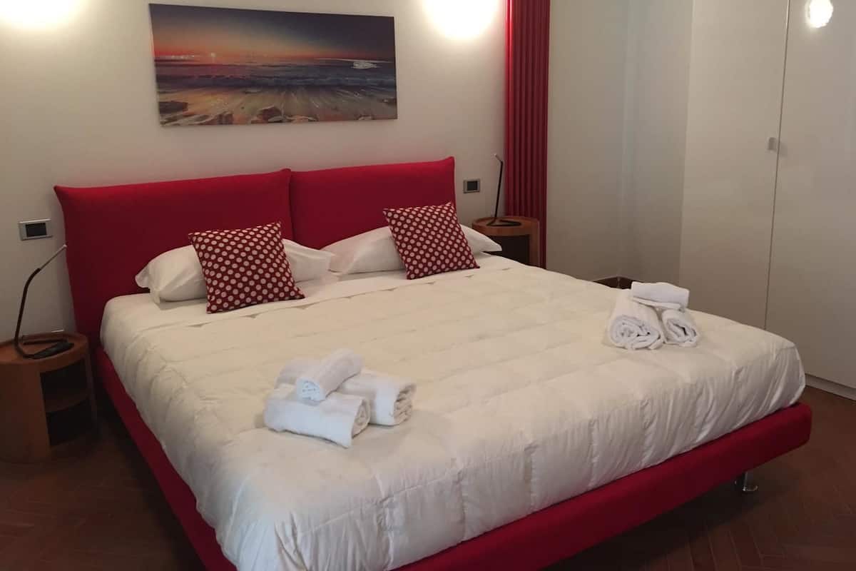 Een hotelkamer met een groot bed, een rood hoofdeinde en een schilderij van een zonsondergang boven de oceaan.