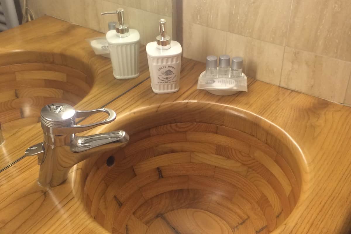 Een houten wastafelmeubel met een chromen kraan en zeepdispensers.