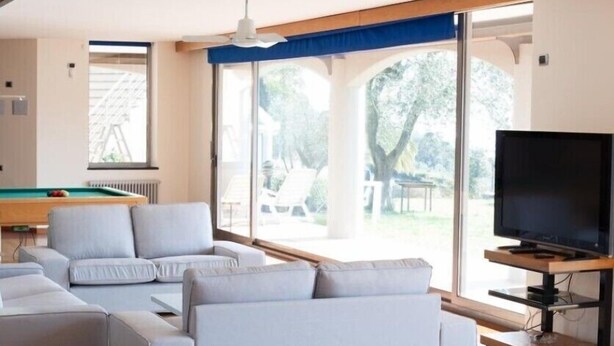 A modern living room with a pool table, a flat-screen TV, and large windows offering a view of the outdoors. - Villa Sofia (La Spezia)