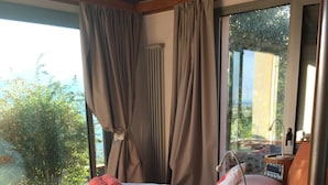 A bedroom with a bed, a bedside table with a lamp, and a view of greenery outside. - Villa Sofia (La Spezia)