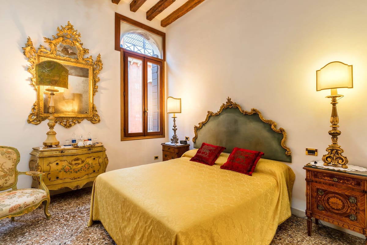 A bedroom with a large bed, ornate furniture, and a window with a view.