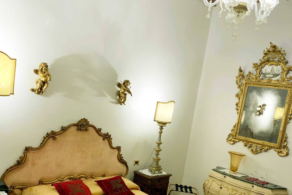 A room with a large bed, a chandelier, a mirror, and a small table with a lamp.