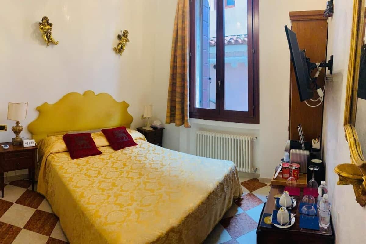 A hotel room with a large bed, a nightstand, a dresser, a window with curtains, and a television mounted on the wall.
