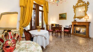 Une pièce avec un lustre, une cheminée, une table entourée de chaises et une fenêtre avec des rideaux.