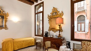 Une pièce comprenant un lit, un bureau, une chaise, une table, une lampe et une fenêtre donnant sur des immeubles.