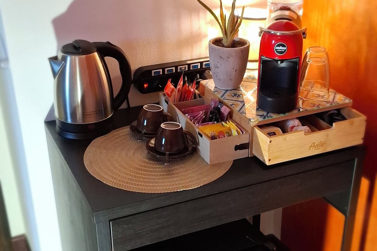 A compact kitchen area with a kettle, coffee maker, and a small potted plant on a table.