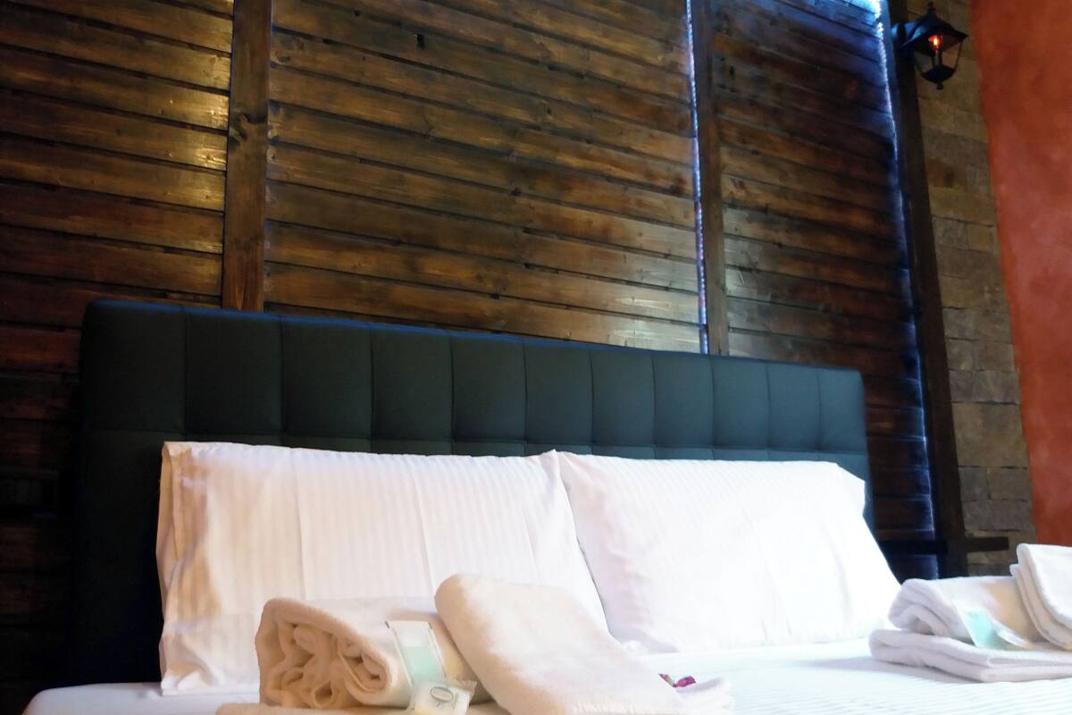 A neatly made bed with white linens, a dark headboard, and a wooden wall behind.