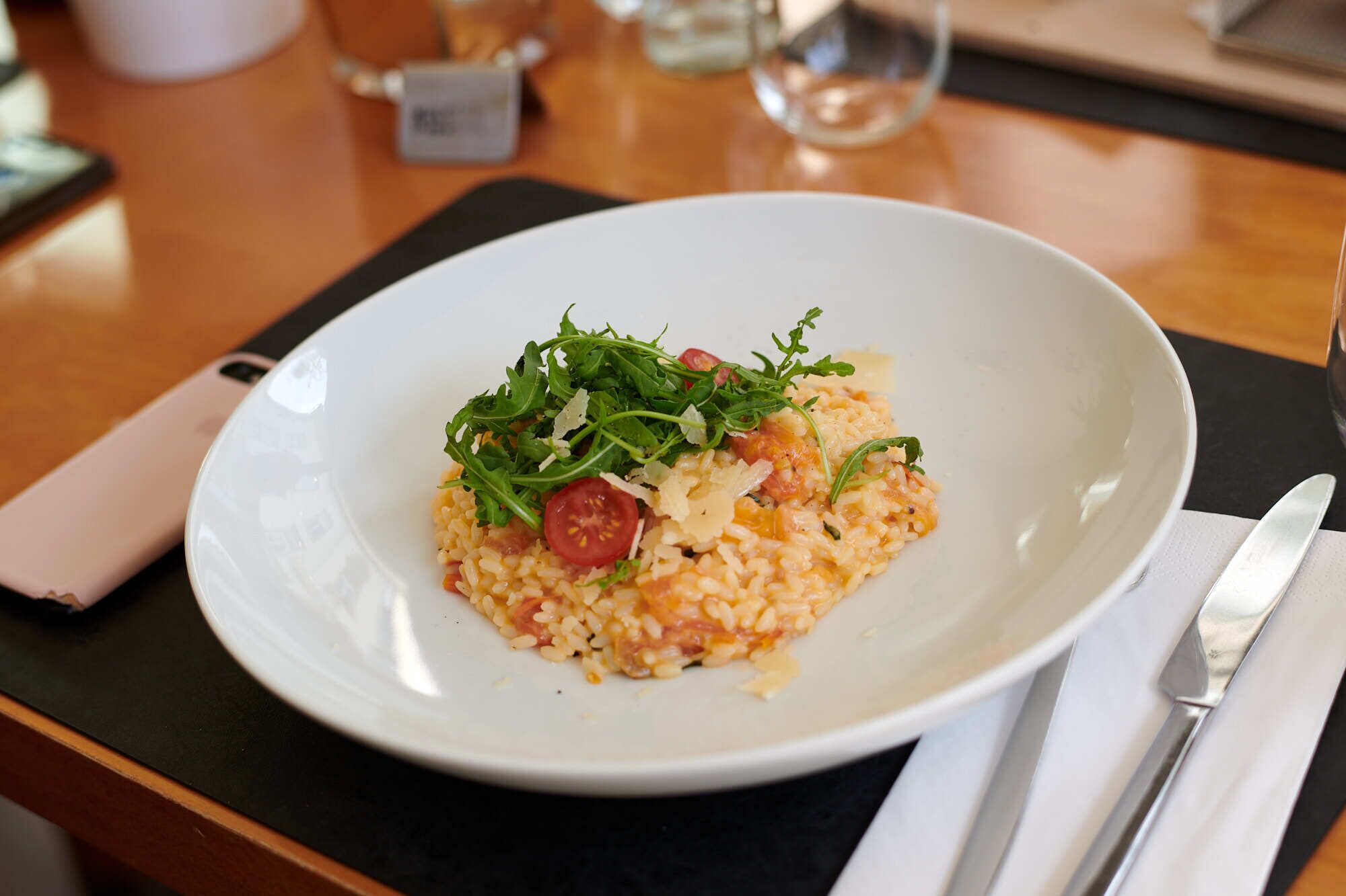 A plate of risotto with arugula and cherry tomatoes on a white plate.