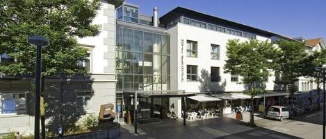 A modern hotel with a glass facade, outdoor seating area, and a bike parking area.