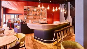 A bar area with a curved counter, wooden chairs, and a shelf with bottles and glasses. - Hotel Berchtold (Burgdorf)