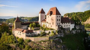 A historic castle with multiple towers, a fortified wall, and a lush surrounding landscape. - Hotel Berchtold (Burgdorf)