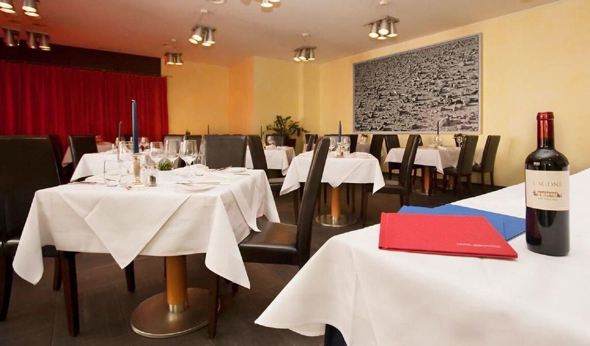 Un restaurante con varias mesas dispuestas para comer, una botella de vino y un menú rojo sobre la mesa.