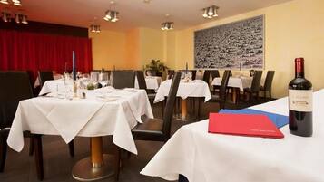 Un restaurante con varias mesas dispuestas para comer, una botella de vino y un menú rojo sobre la mesa.