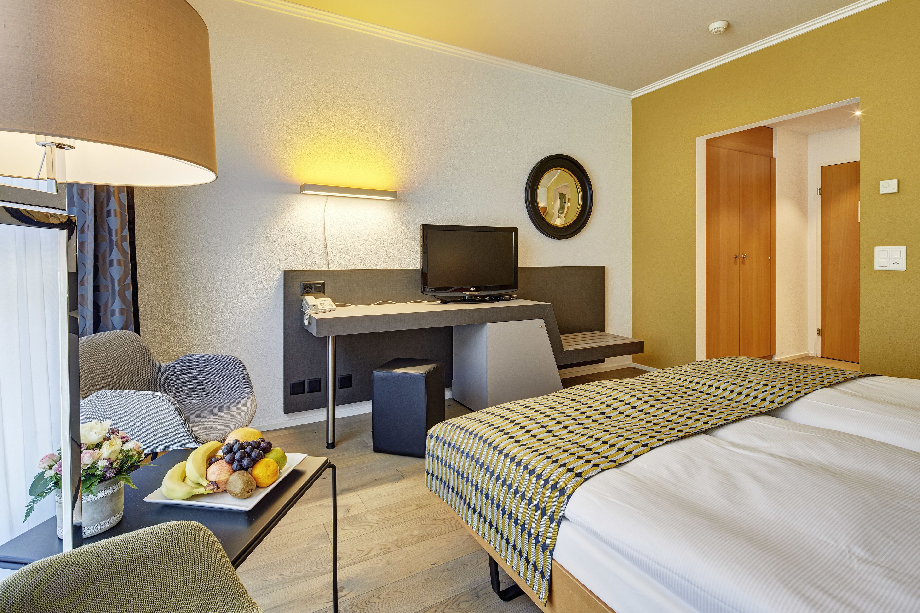 Una habitación de hotel con cama, escritorio, silla, televisor y frutero.