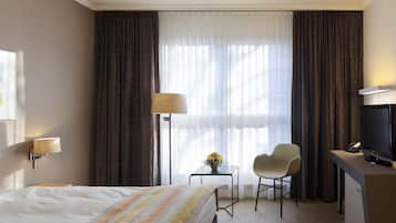 A hotel room with a bed, a desk, a chair, a TV, and a window with curtains.