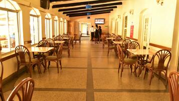 Un restaurante con sillas y mesas de madera, una pantalla de televisión y piso de baldosas.
