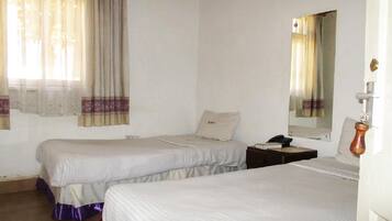 A room with two beds, a nightstand, a mirror, and a window with curtains.