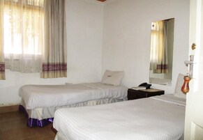 A room with two beds, a nightstand, a mirror, and a window with curtains.