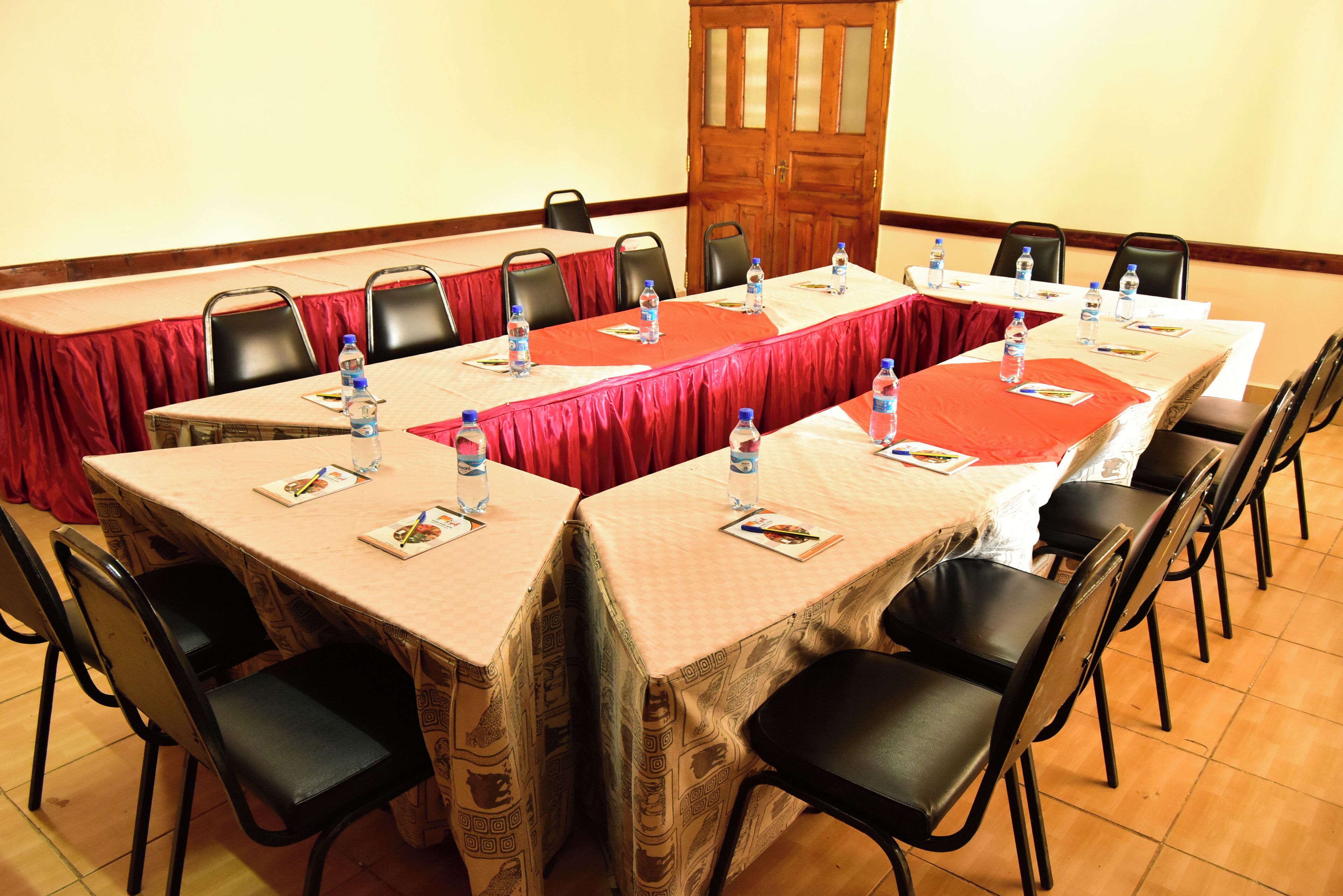 Une salle de conférence avec de longues tables, des chaises noires et des bouteilles d’eau sur chaque table.