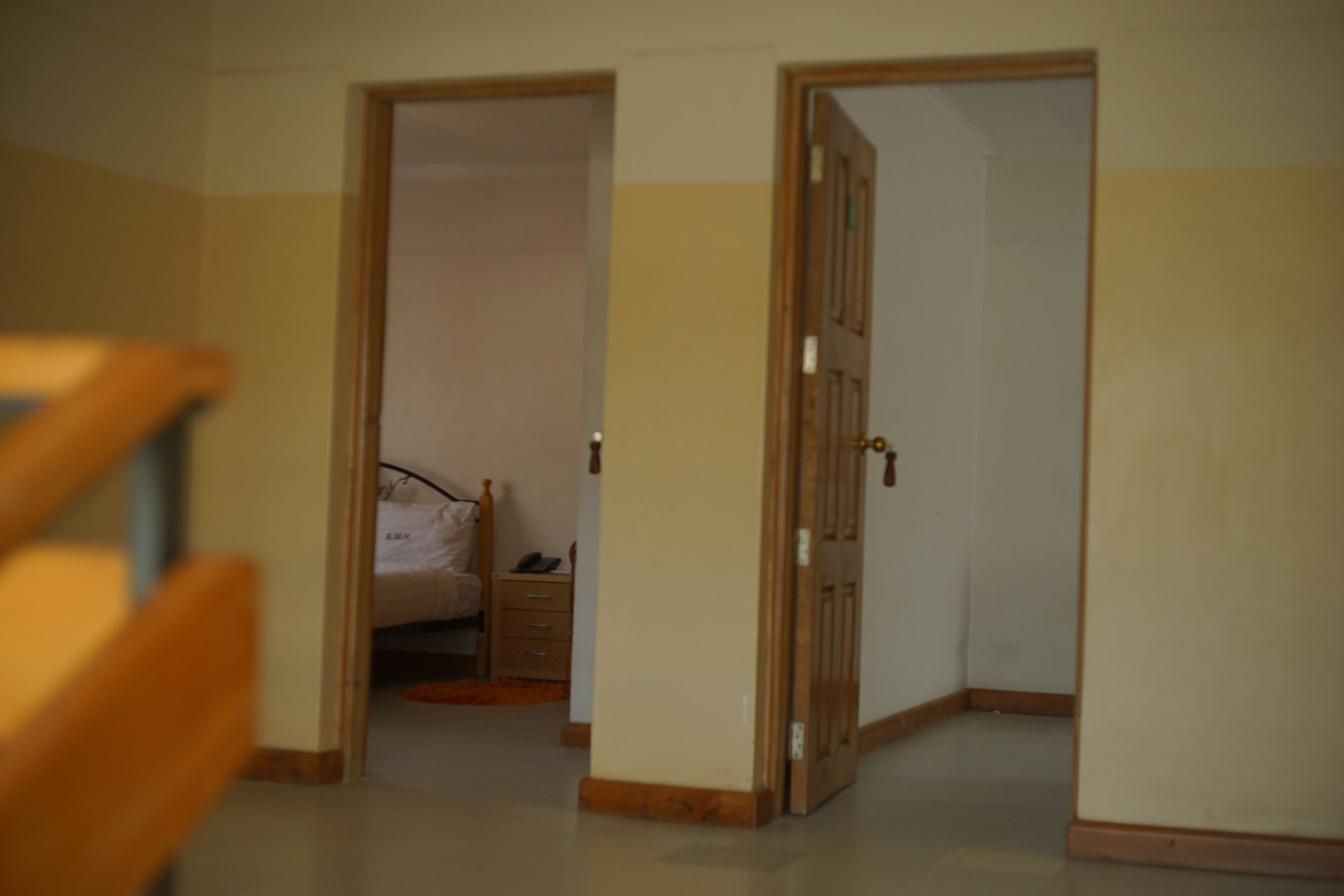 Una habitació amb un llit, una tauleta de nit i una porta que dona a una altra habitació.