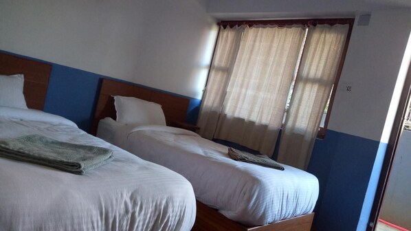 Una habitación de hotel con dos camas individuales, una ventana con cortinas y un cabecero de madera.