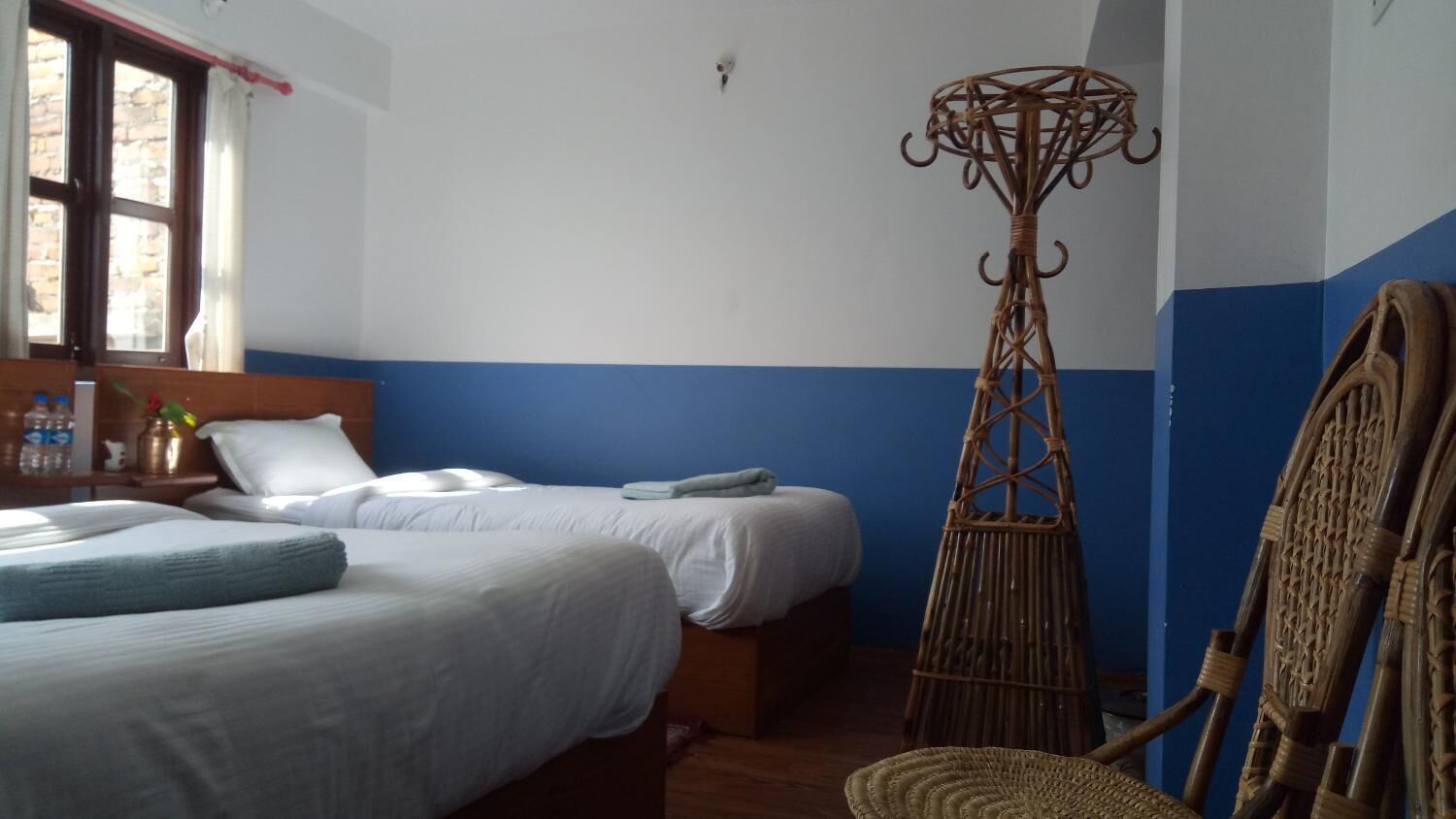 A bedroom with two beds, a window, a wall-mounted shelf, and a woven chair.