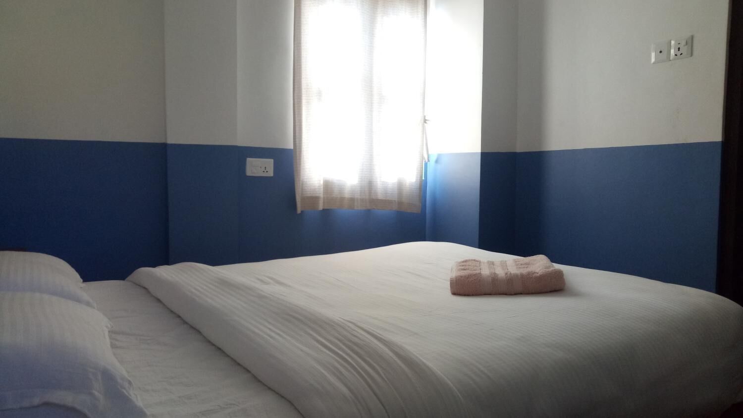 A hotel room with a bed, a window with curtains, and a wall switch.
