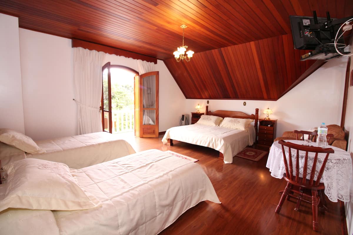Ein Schlafzimmer mit zwei Betten, einer Holzbalkendecke, einem Esstisch mit Stühlen und einem an der Wand befestigten Fernseher.