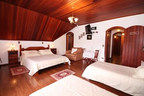 A bedroom with two beds, wooden flooring, a chandelier, a television, and a small table with chairs.