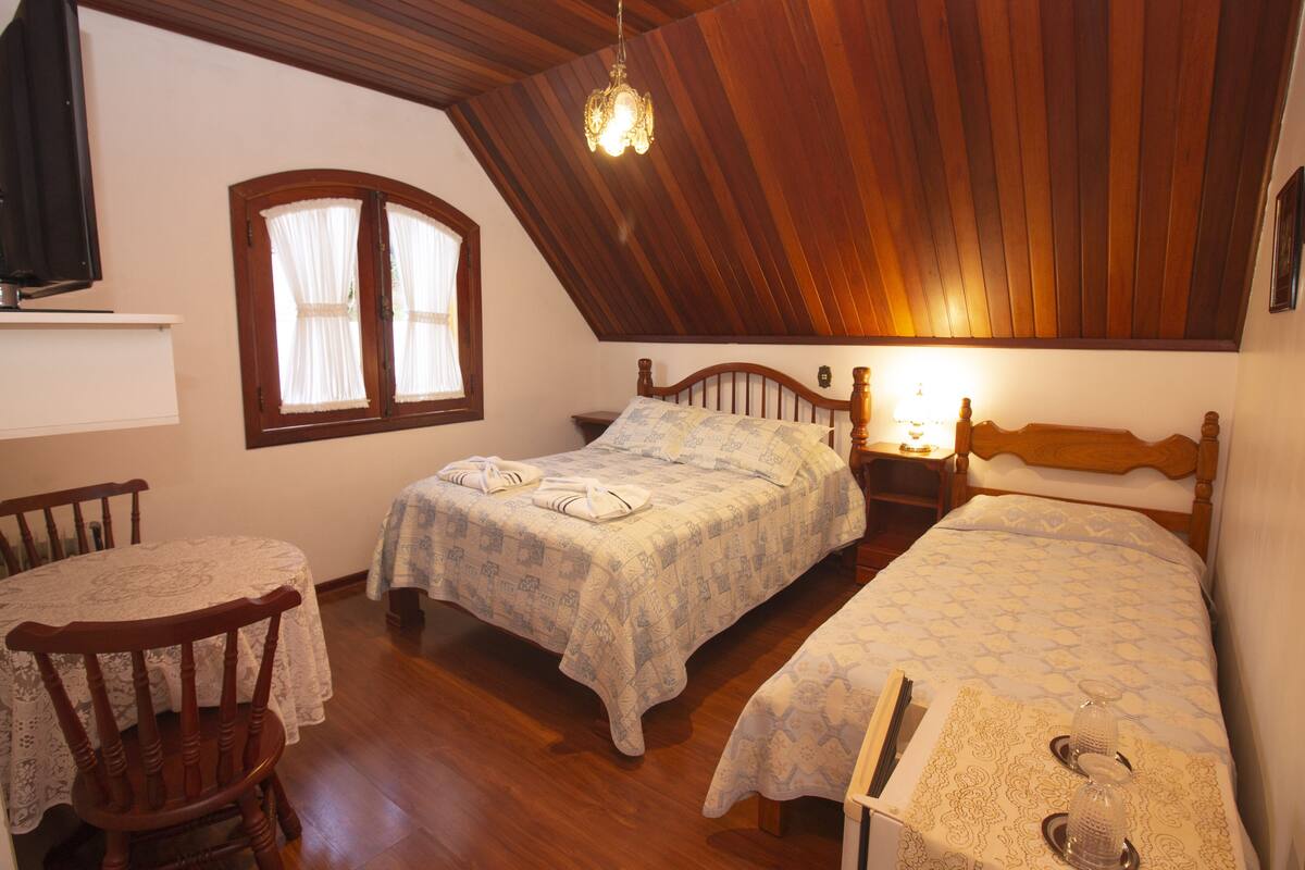 Ein Zimmer mit zwei Betten, Holzboden, einem Fenster mit Vorhängen, einem Tisch mit Stuhl und einer Chandelier.