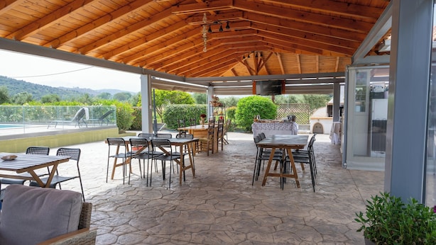 A covered outdoor patio with stone flooring, wooden furniture, and a view of the countryside. - Spedion Villa Gytheio (East Mani)