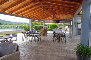 Une terrasse extérieure couverte, dotée d’un sol en pierre, de meubles en bois et offrant une vue sur la campagne.
