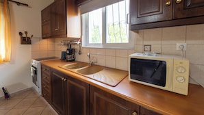 A kitchen with wooden cabinets, a sink, a microwave, and a window with a view of greenery. - Spedion Villa Gytheio (East Mani)