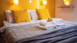 A neatly made bed with white and yellow pillows, a folded towel, and a small flower on the bed. - Spedion Villa Gytheio (East Mani)