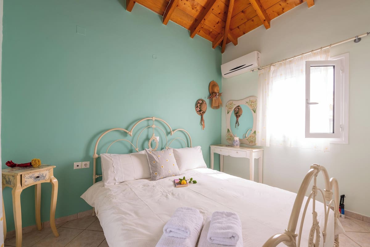 Une chambre à coucher comprenant un lit, une table de chevet, une commode, une fenêtre avec des rideaux et un appareil de climatisation.