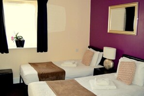 A hotel room with two beds, a window with curtains, a potted plant, a bedside table with a lamp, and a mirror on the wall. - the orchard hotel (Quedgeley)