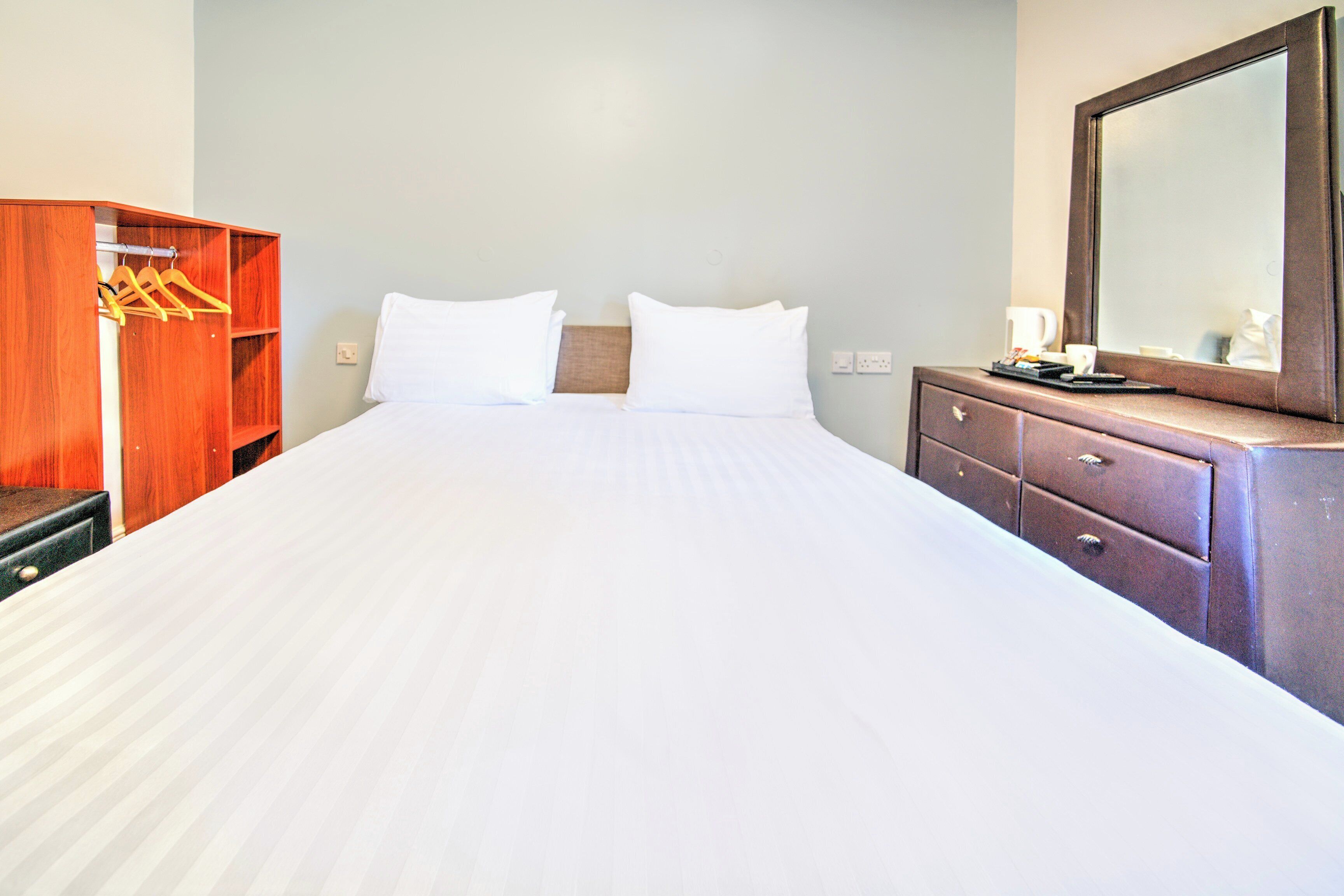 Habitación de hotel con una cama grande, armario de madera y cómoda con espejo.