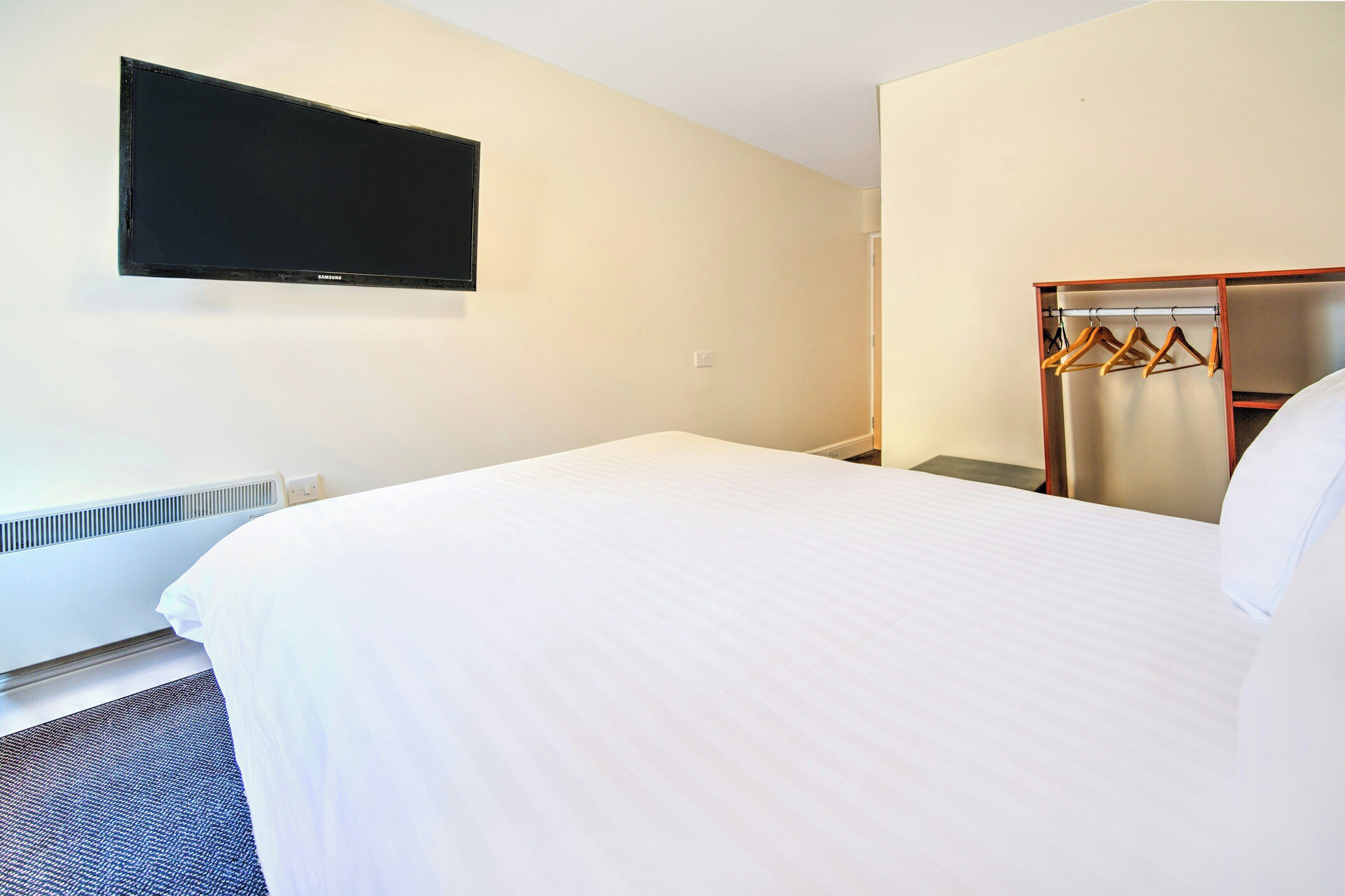 A hotel room with a bed, a television mounted on the wall, and a wardrobe with hangers.