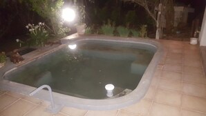 Una piscina scoperta rettangolare con bordo piastrellato, un rubinetto e una fonte di luce sullo sfondo.