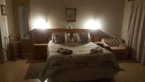 Camera d'albergo con un letto grande, due lampade sui comodini, un comodino in legno, una sedia e una scrivania.