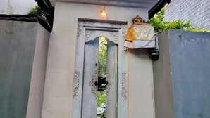 A traditional gate with intricate carvings, a small shelf with a decorative item, and a potted plant beside it. - WOODEN Home Top LOCATION in Seminyak Near Beach, Shops, Restaurants (seminyak)