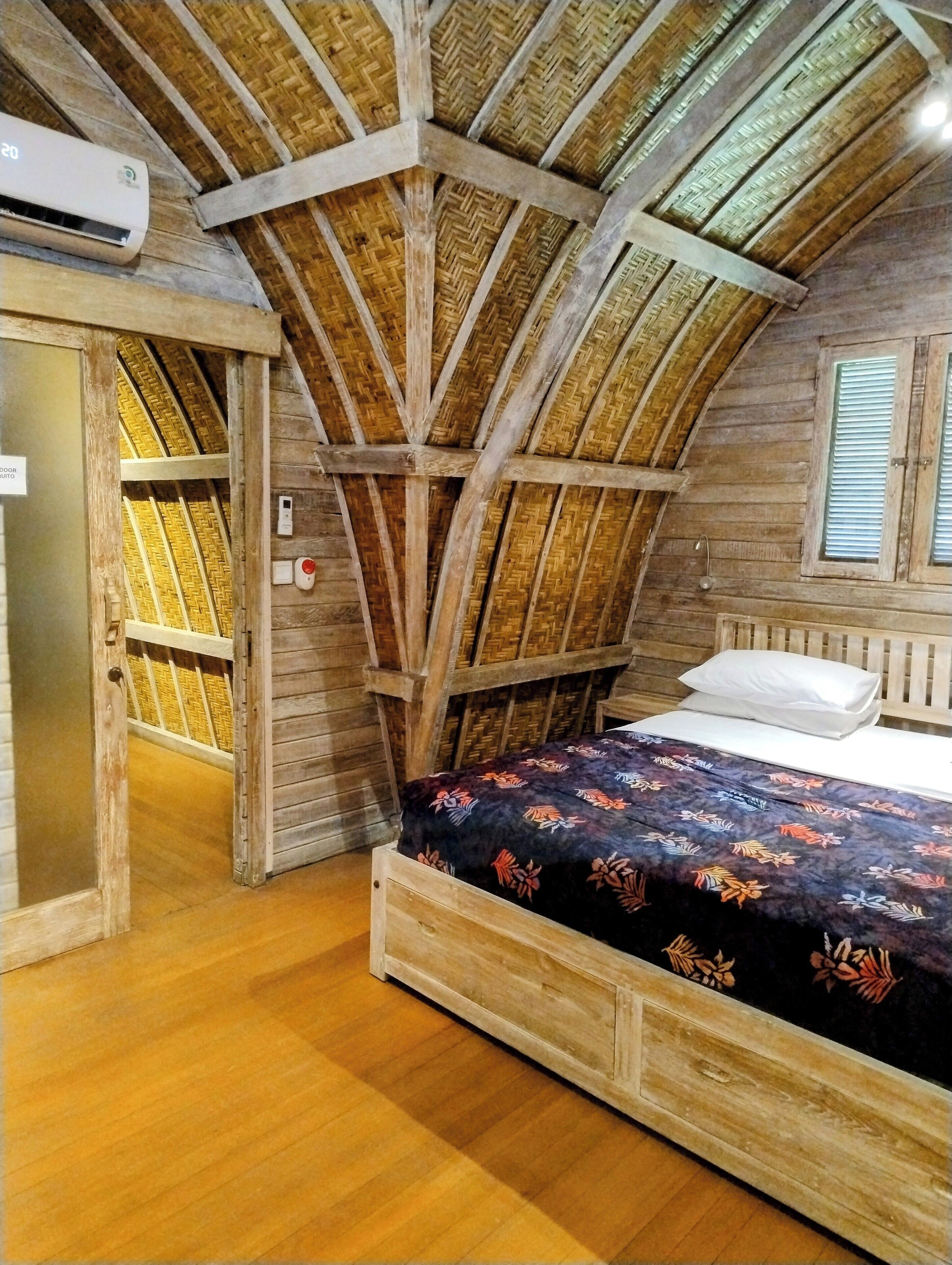 A rustic room with a wooden bed, a door leading to a balcony, and a woven ceiling.