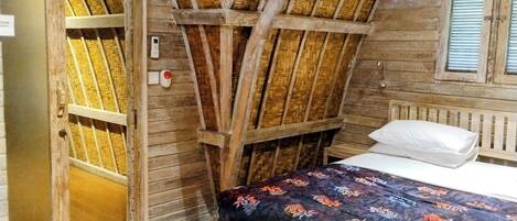 A rustic room with a wooden bed, a door leading to a balcony, and a woven ceiling.