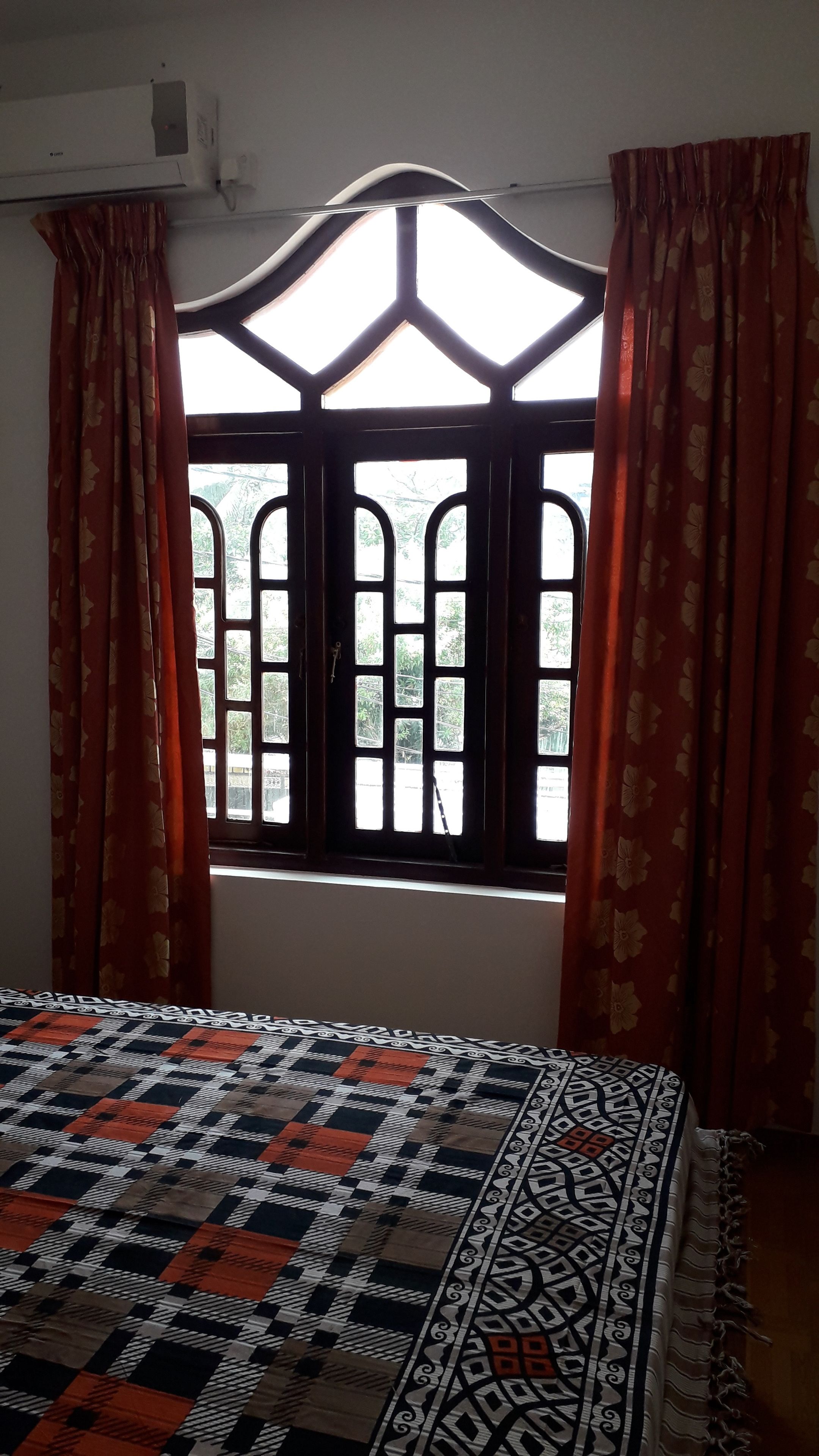 A room with a bed, a window with curtains, and an air conditioning unit.