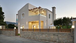 A modern two-story house with a stone wall entrance, a wooden fence, and a balcony with a pergola. - Villa Despina in Kissamos (Kissamos)