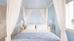 A four-poster canopy bed with white curtains, two bedside tables with lamps, and a view of the outdoors through a window. - Villa Despina in Kissamos (Kissamos)