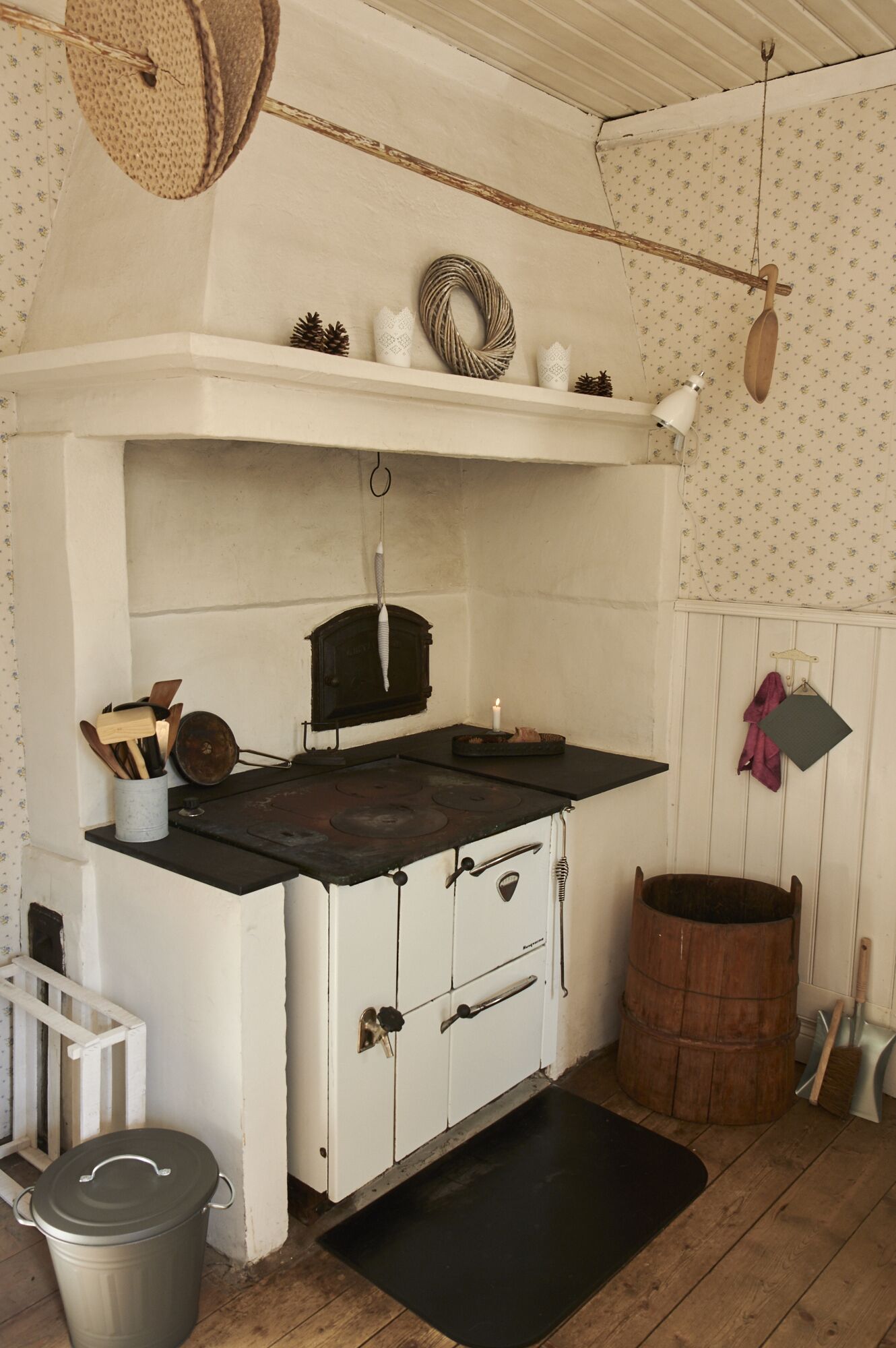 Een landelijke keuken met een houtkachel, witte kasten en een hangende pannendroger.
